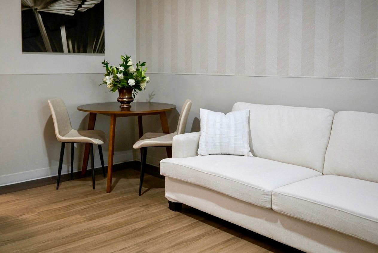 Minimal living room with white sofa, small wooden table, chairs, and flower vase on wood floor