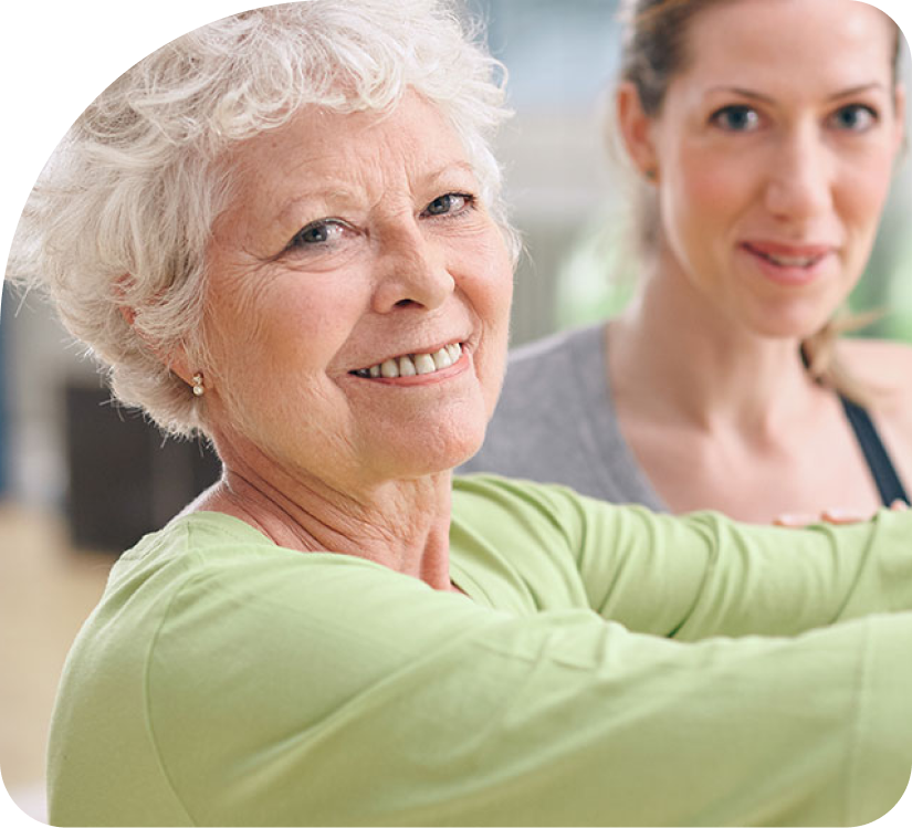Older woman smiling while stretching with a trainer in a bright exercise studio
