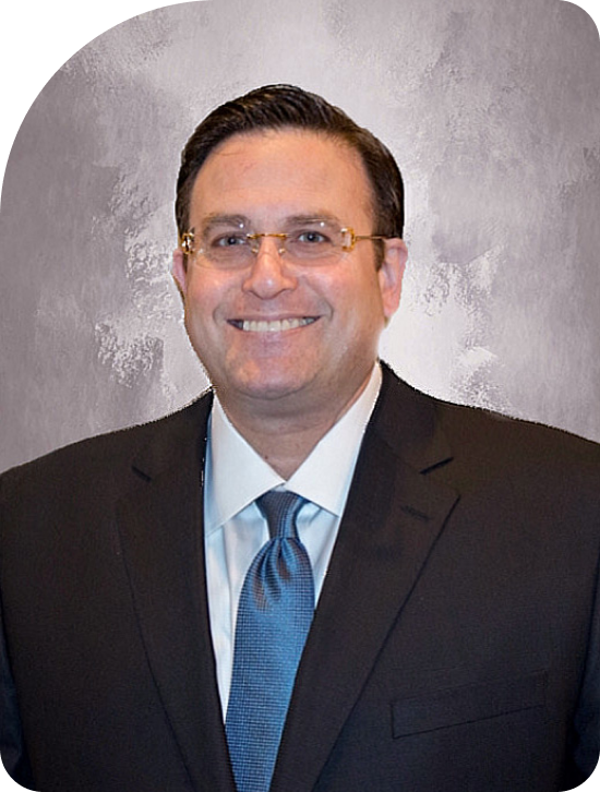Portrait of a smiling man in a dark suit, blue tie, and glasses against a gray backdrop