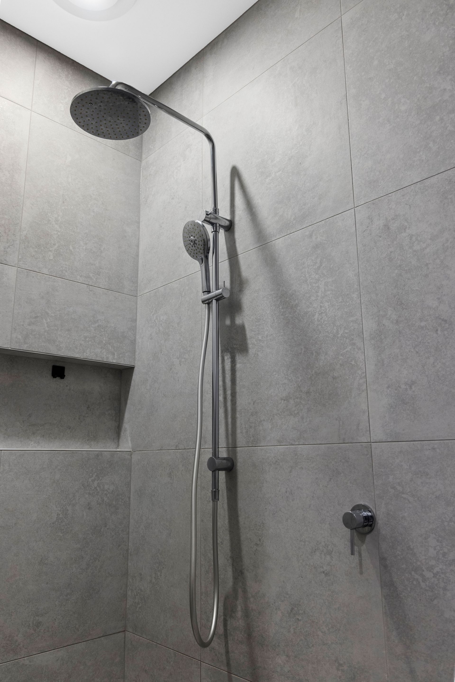 Shower with gray tile walls and chrome fixtures.