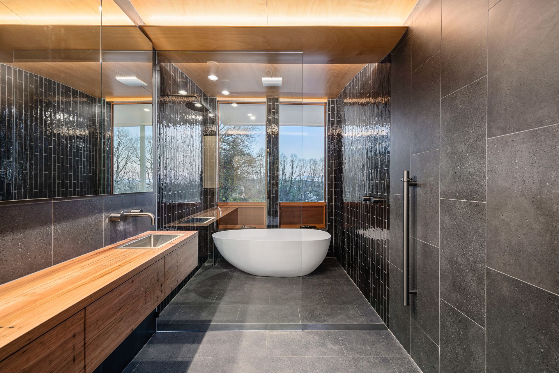 Modern bathroom with black tiled walls, a wooden vanity, and a white soaking tub— Croker Plumbing and Gas in Goulburn, NSW