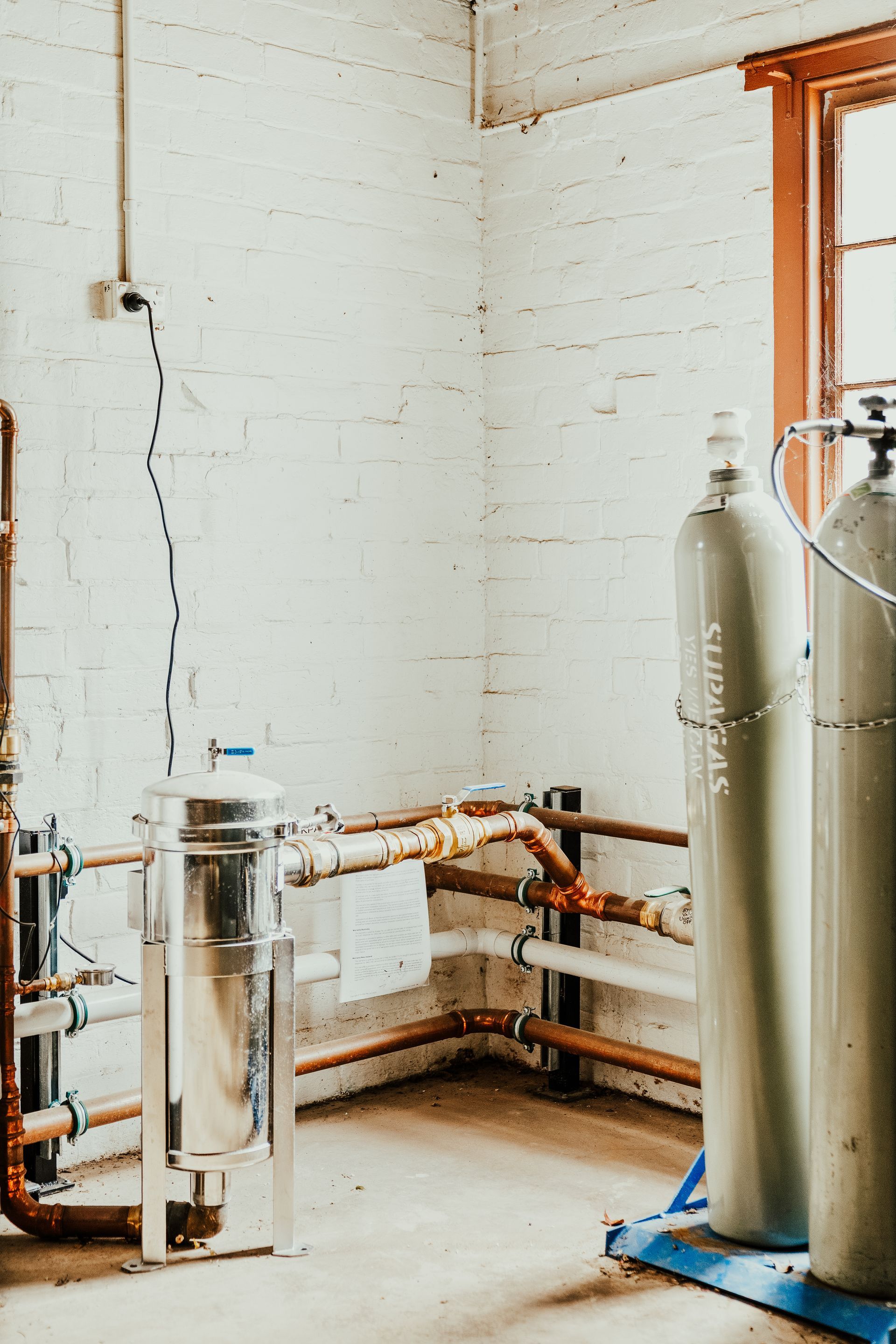 Industrial room with equipment, metal tanks, copper pipes, and a window.