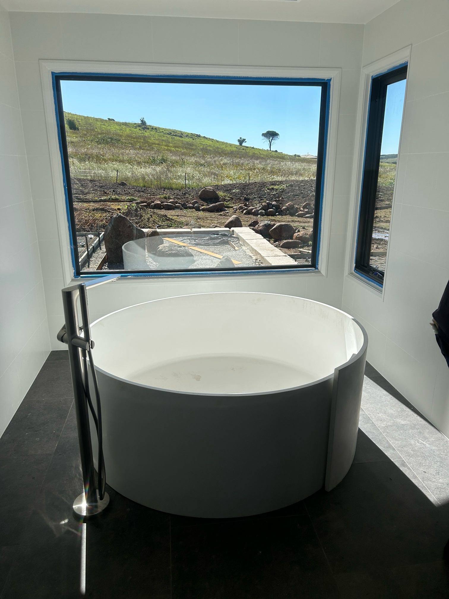 Round white bathtub in bathroom with large window overlooking a field.