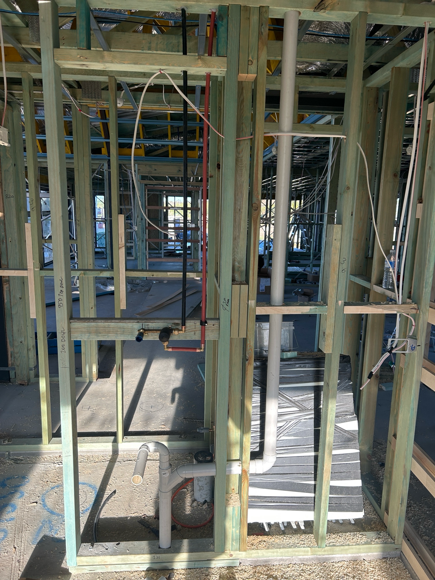 Wooden frame construction of a building interior with exposed pipes and wiring.