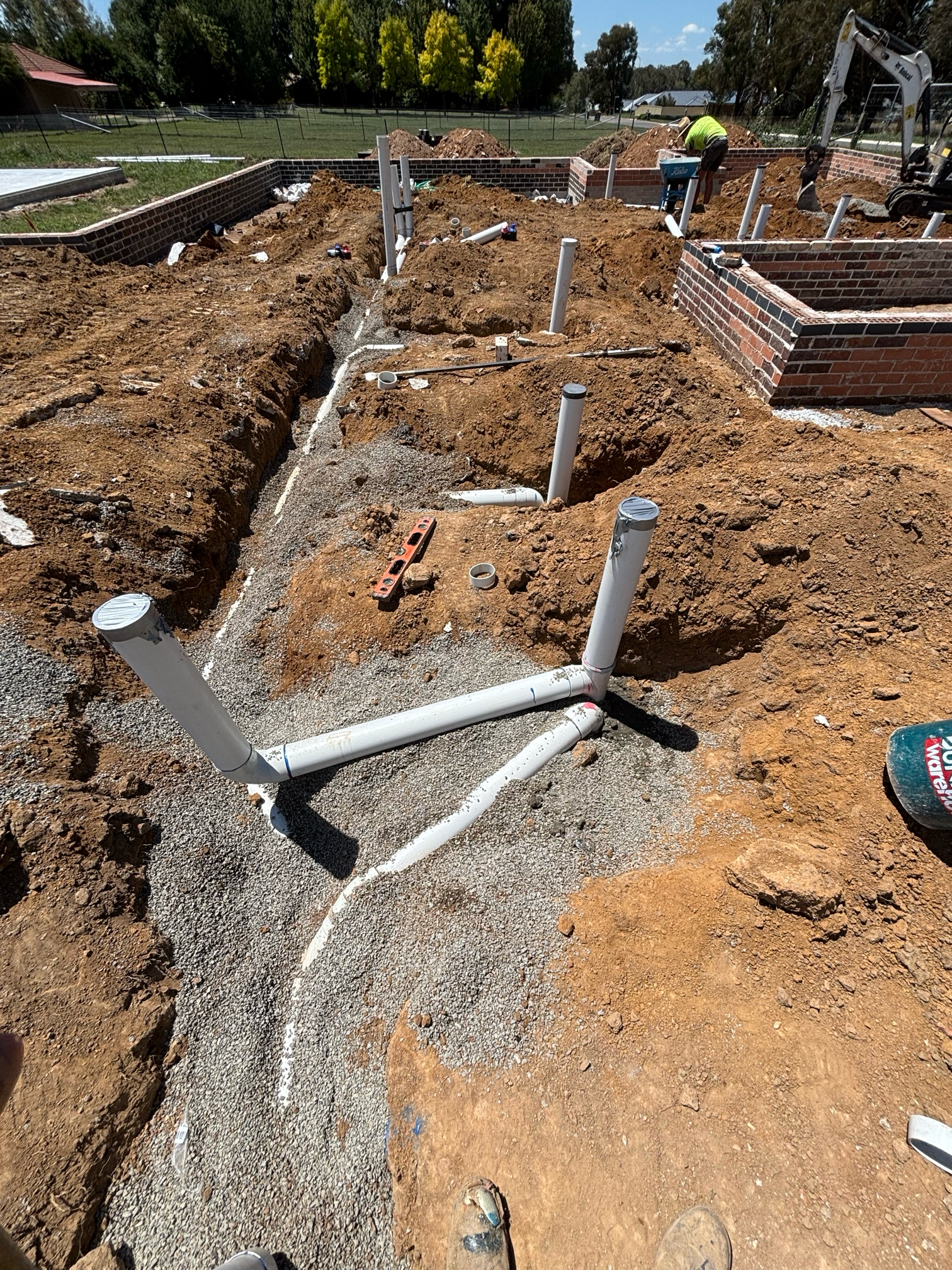 Construction site with plumbing pipes in trenches; brick foundation walls.
