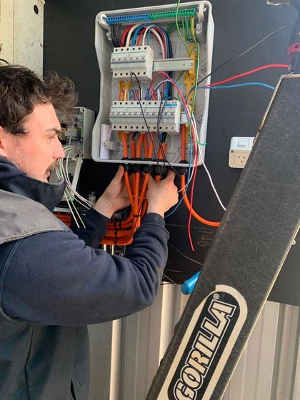 Technician wiring an open electrical panel with orange cables in a workshop.