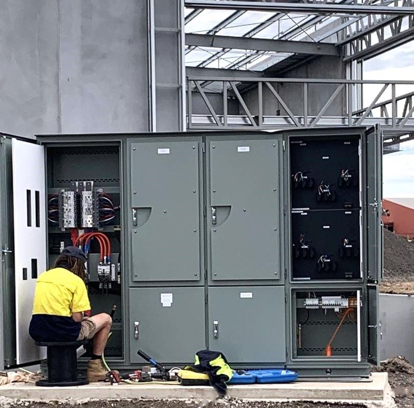 Technician in yellow shirt working on an open electrical control cabinet at a construction site