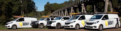 Five white NSW taxis parked in a row outdoors, with trees and a building in the background