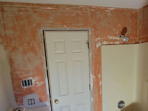 A bathroom with a white door and a shower that had wallpaper removed.