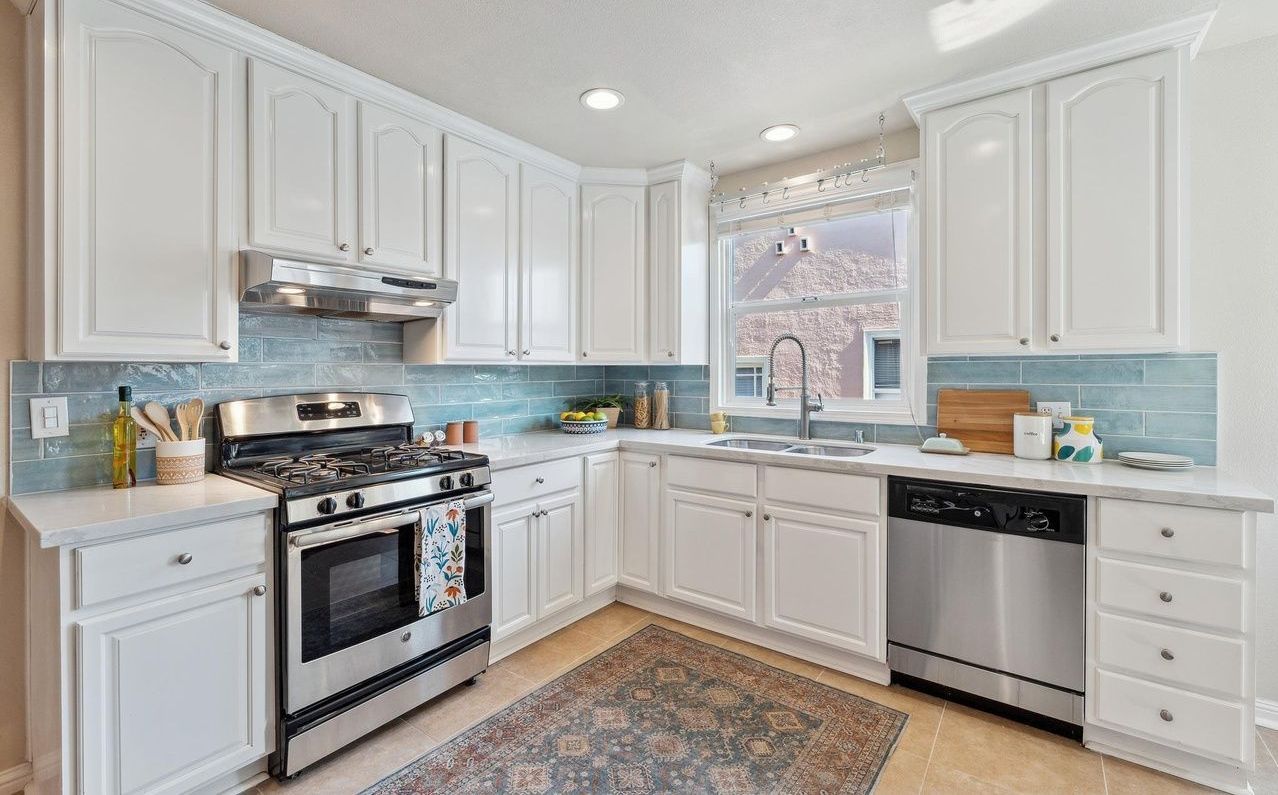 A kitchen with white cabinets , stainless steel appliances , and a rug.