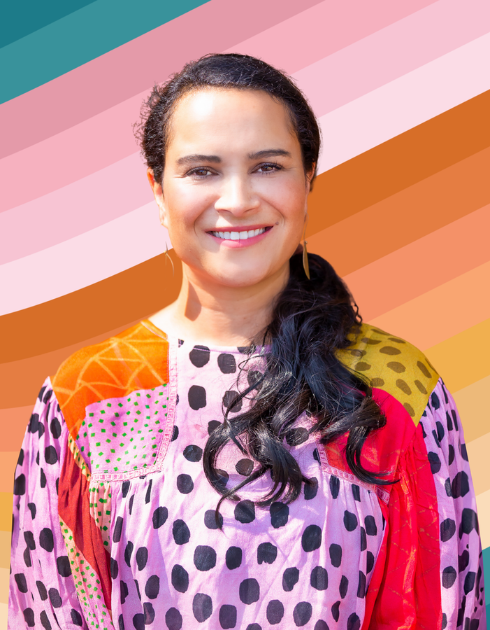 A woman in a polka dot dress is smiling in front of a colorful background.