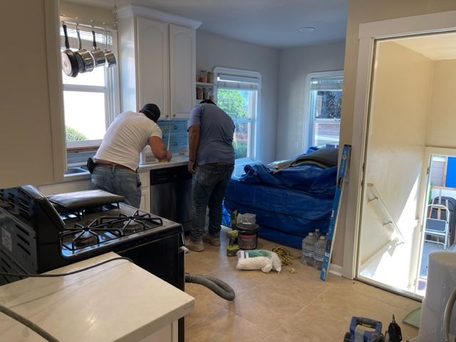 Two men are working in a kitchen with a blue tarp on the floor.