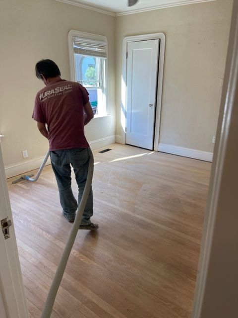 A man is vacuuming a wooden floor in a room.