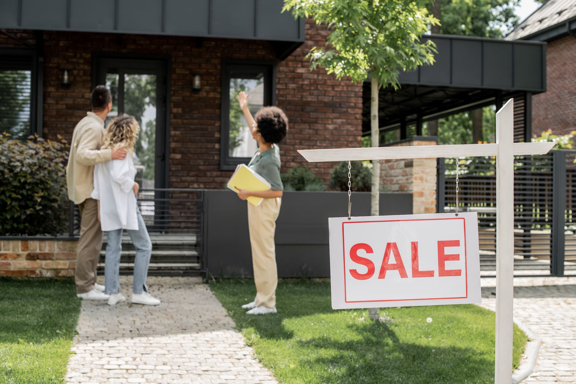 A woman is standing in front of a house with a for sale sign.