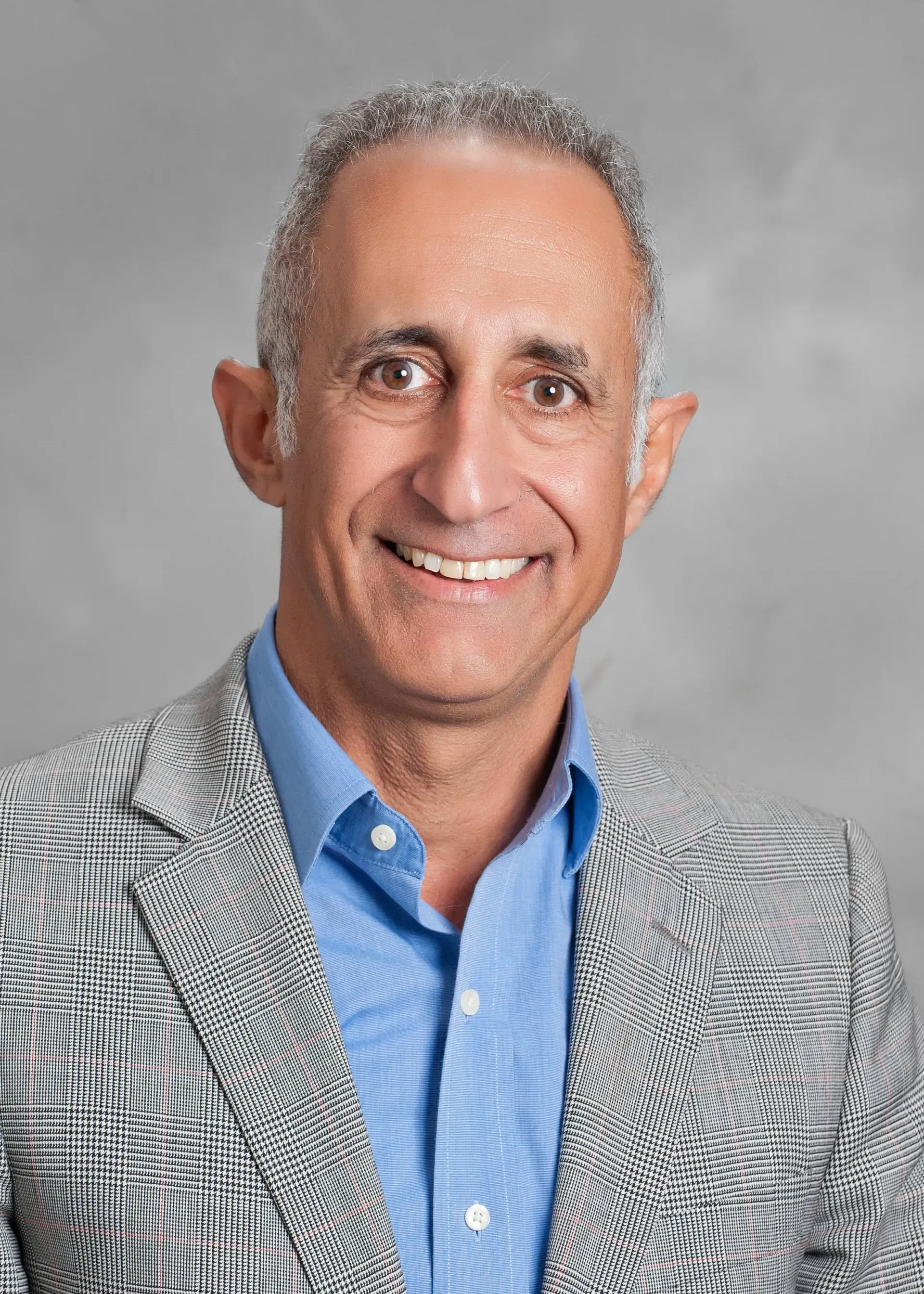 Smiling man in a gray patterned blazer and blue shirt against a gray background Smiling man in a gray patterned blazer and blue shirt against a gray background