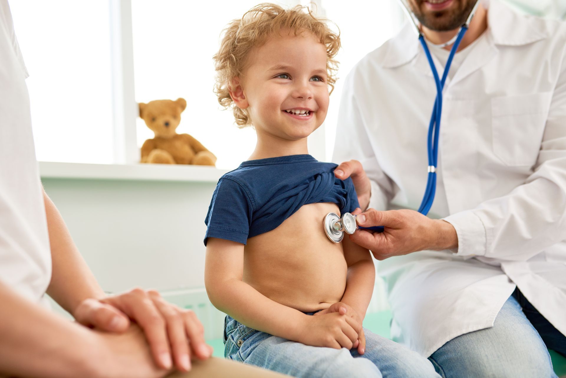 Child smiling as a doctor listens to their chest in a bright clinic room