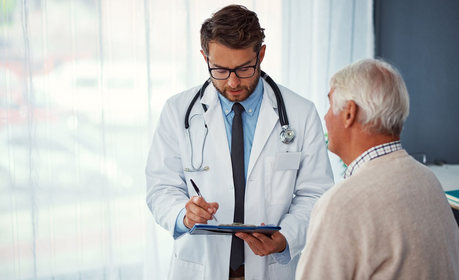 Doctor in white coat taking notes on a clipboard while talking with a patient in a clinic Doctor in white coat taking notes on a clipboard while talking with a patient in a clinic