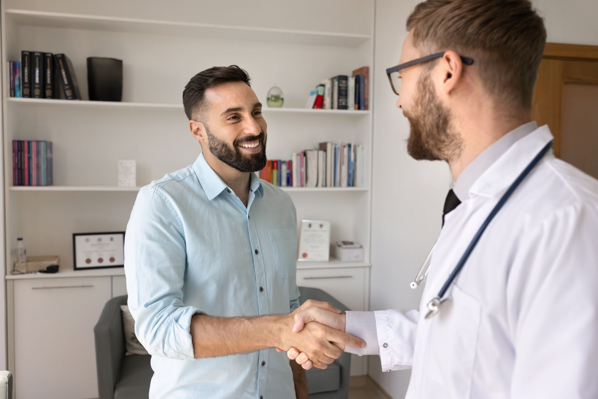 Two men shaking hands in a bright office with shelves in the background Two men shaking hands in a bright office with shelves in the background