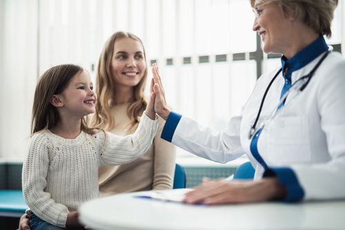 Doctor smiling with a child and parent in a bright clinic, high-fiving across the desk Doctor smiling with a child and parent in a bright clinic, high-fiving across the desk
