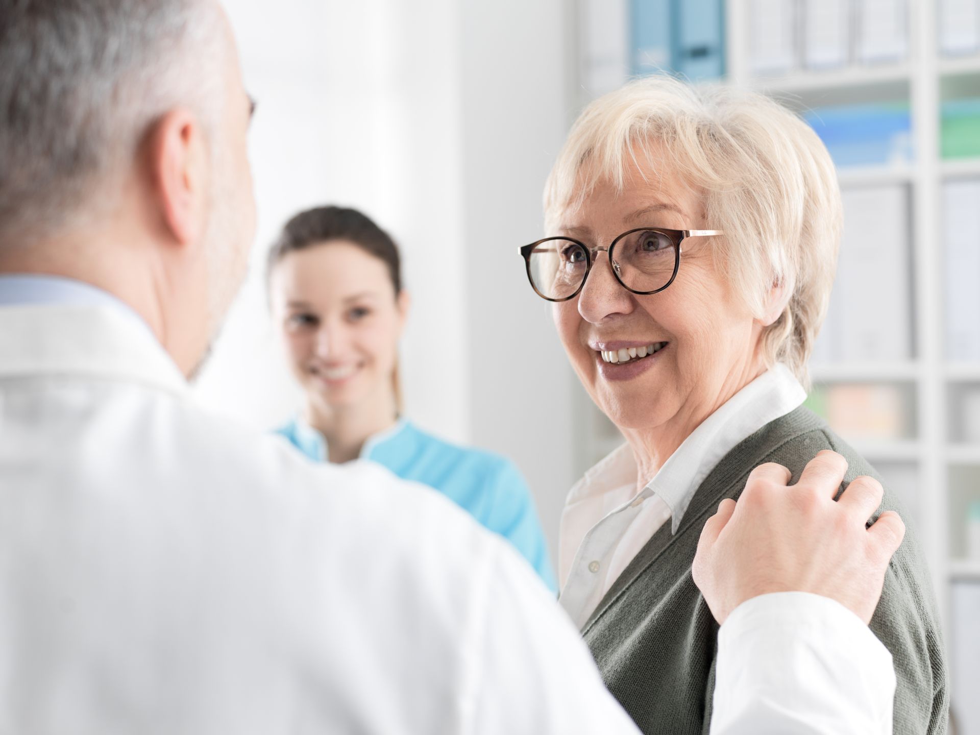 Doctor comforting smiling patient in a bright clinic, with a nurse in the background Doctor comforting smiling patient in a bright clinic, with a nurse in the background