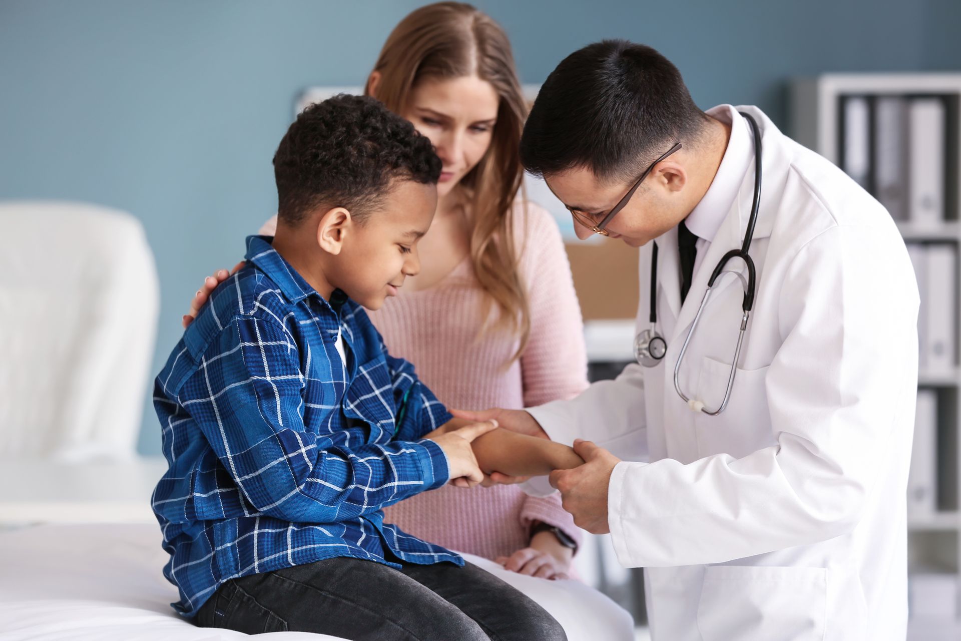 Doctor examining a boy’s hand while a woman watches nearby in a bright clinic room