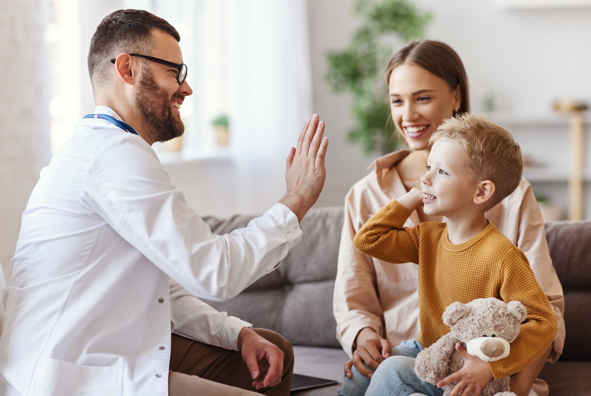 Doctor giving a high-five to a child while speaking with a smiling parent in a clinic.