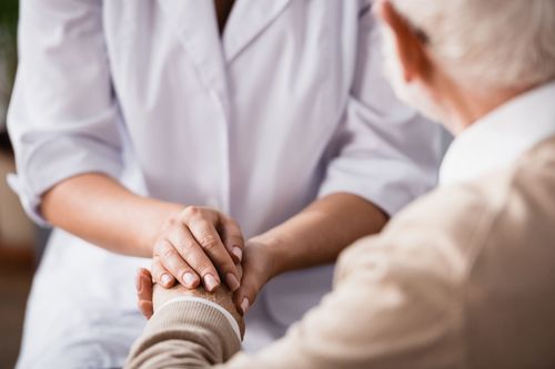 Healthcare worker holding an elderly patient’s hand in a comforting visit Healthcare worker holding an elderly patient’s hand in a comforting visit