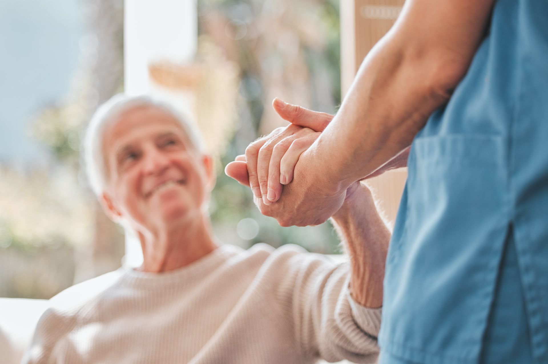Caregiver holding an older adult’s hand in a bright, supportive care setting