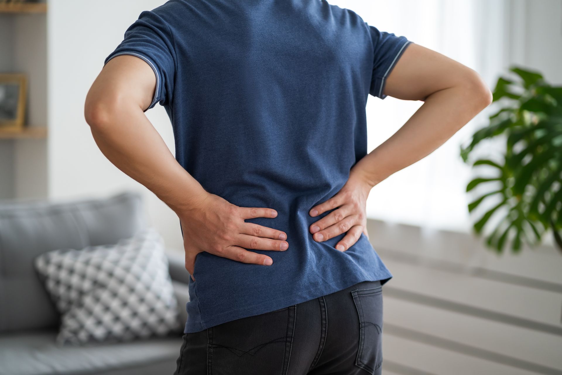 Person holding lower back in a living room, suggesting back pain