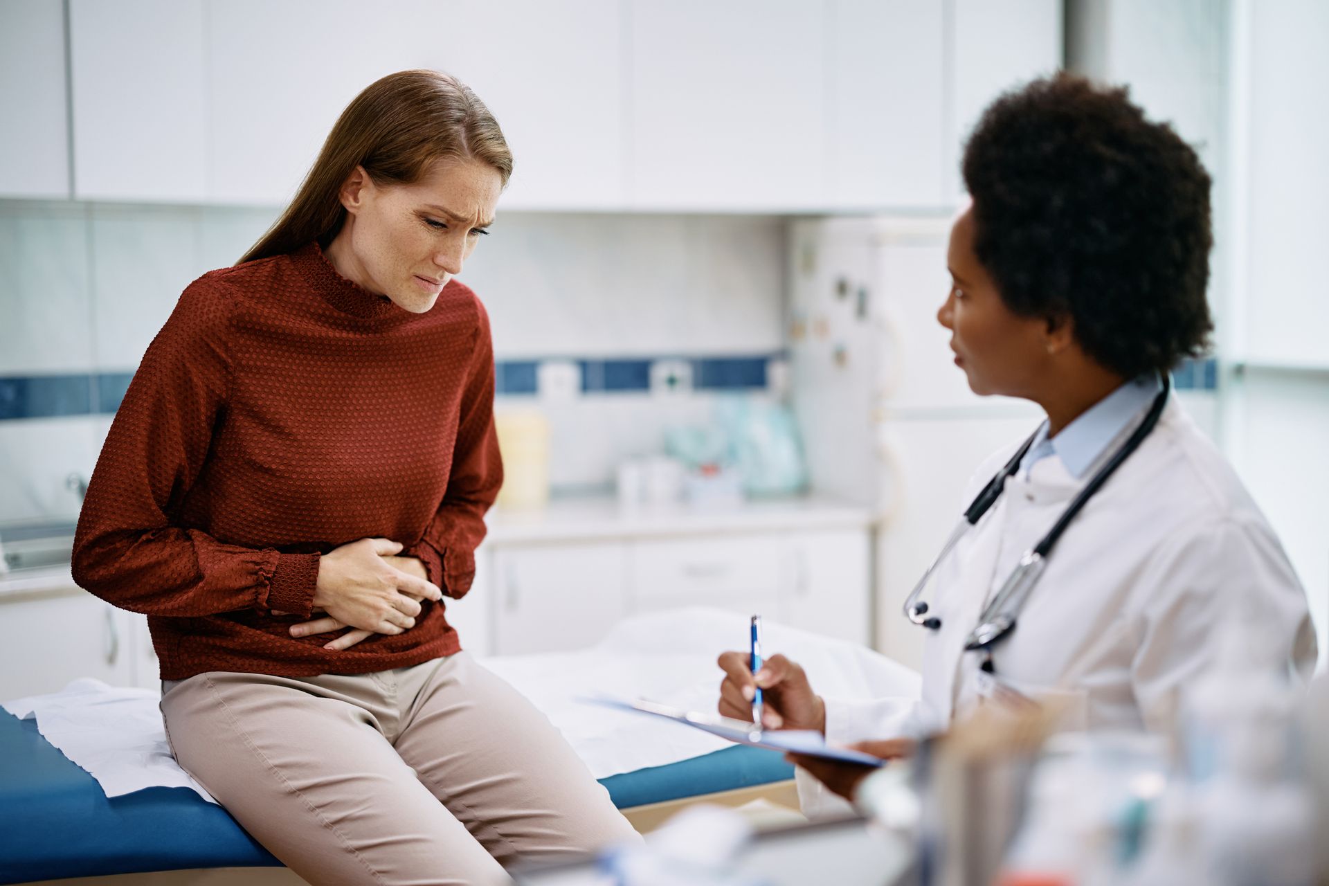Doctor consulting with a patient holding her stomach in a clinic exam room Doctor consulting with a patient holding her stomach in a clinic exam room