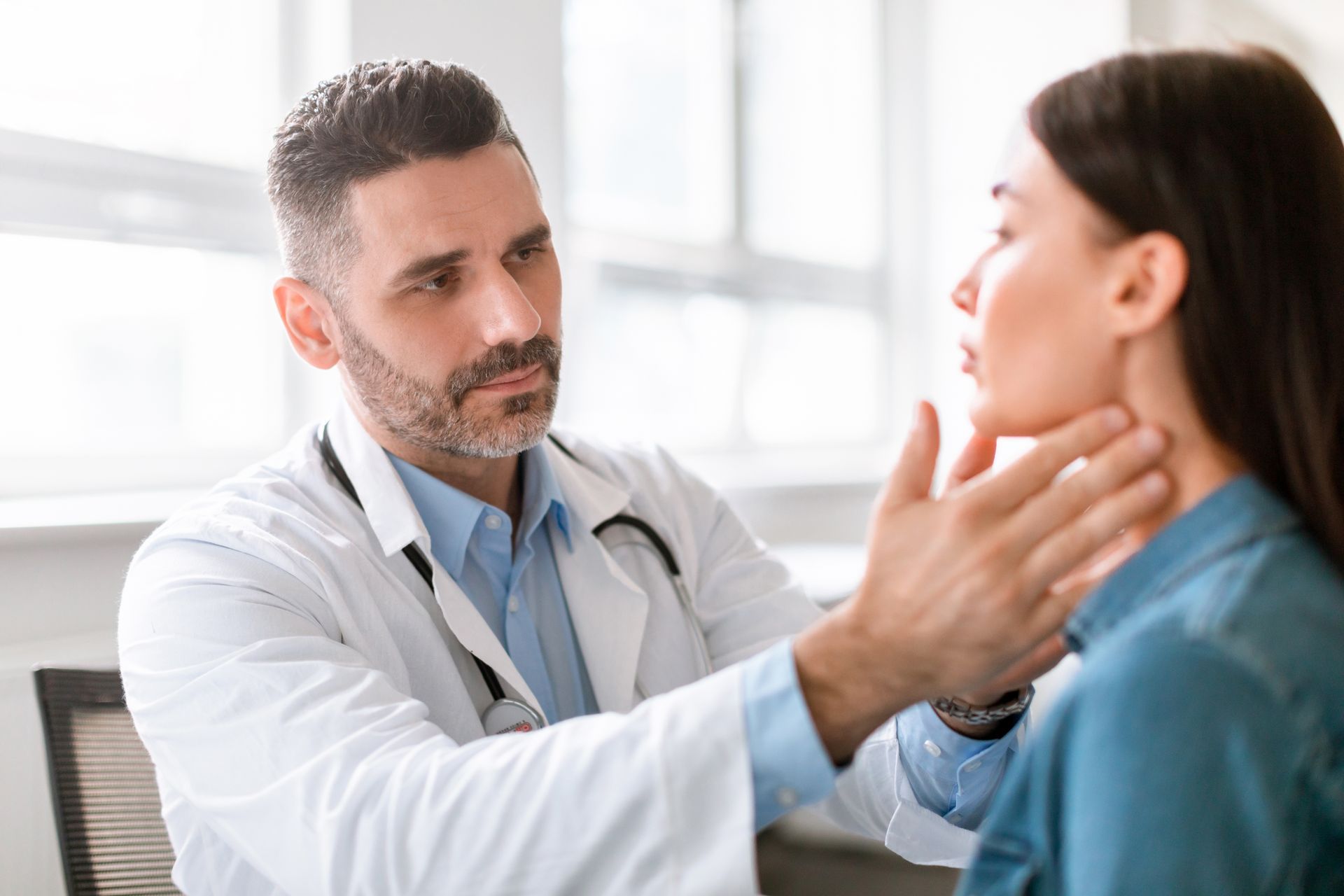 Doctor examining a patient’s neck in a bright clinic room Doctor examining a patient’s neck in a bright clinic room