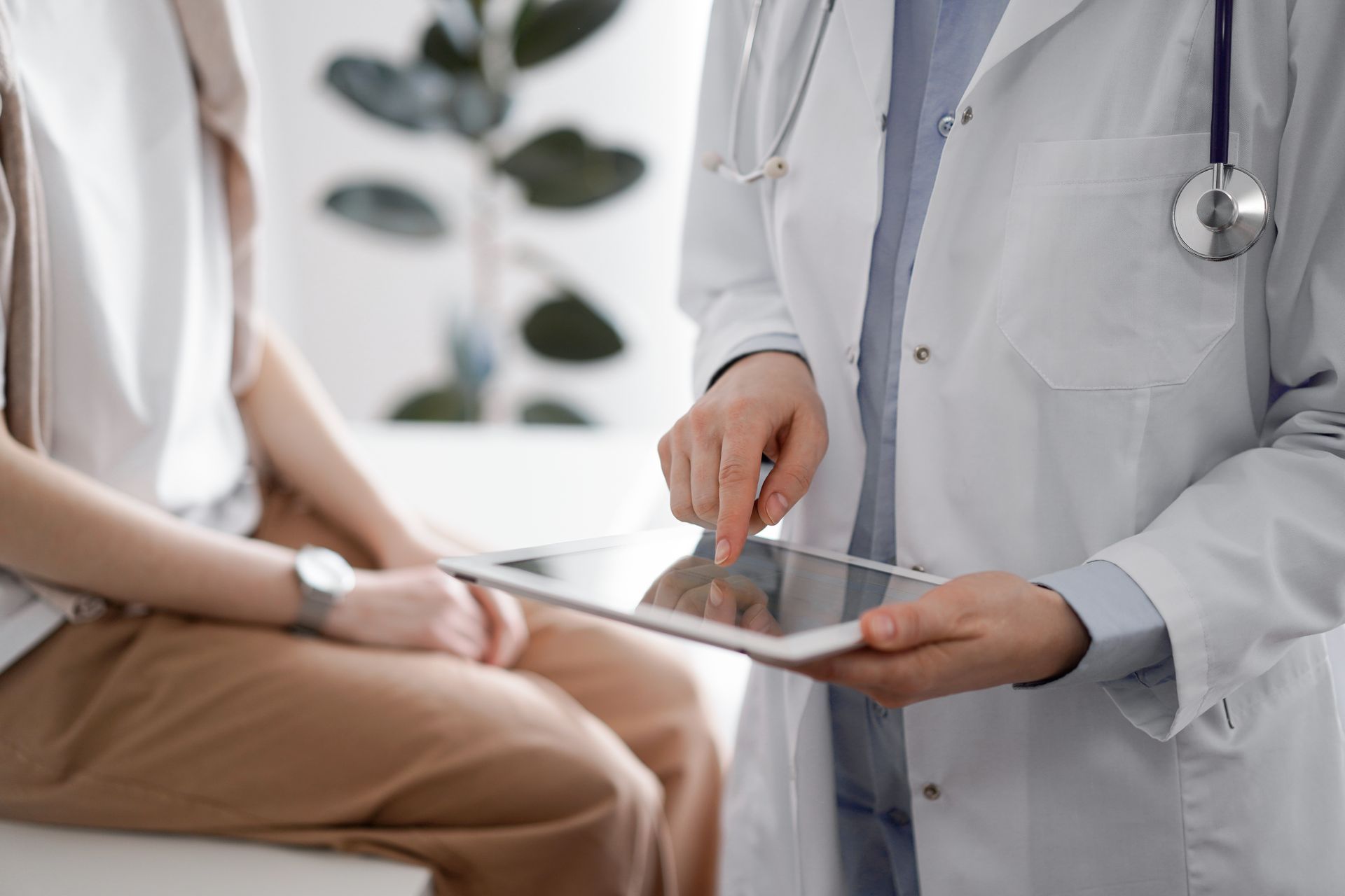 Doctor pointing at a tablet while speaking with a seated patient in a clinic Doctor pointing at a tablet while speaking with a seated patient in a clinic