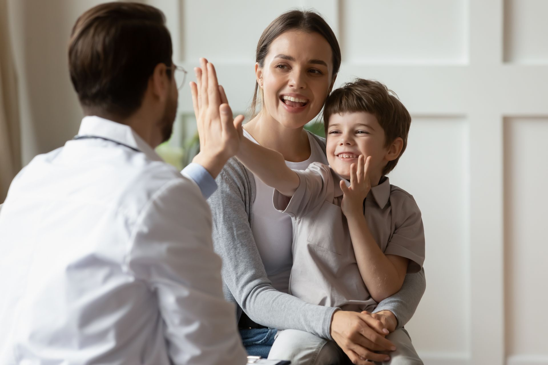 Doctor high-fiving a smiling parent holding a child in a bright clinic room Doctor high-fiving a smiling parent holding a child in a bright clinic room