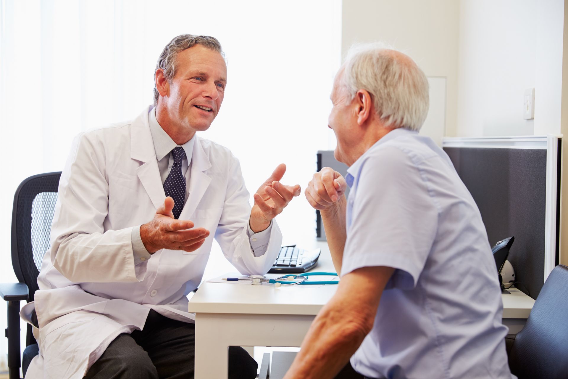 Doctor speaking with a patient in a bright office, gesturing across a desk.