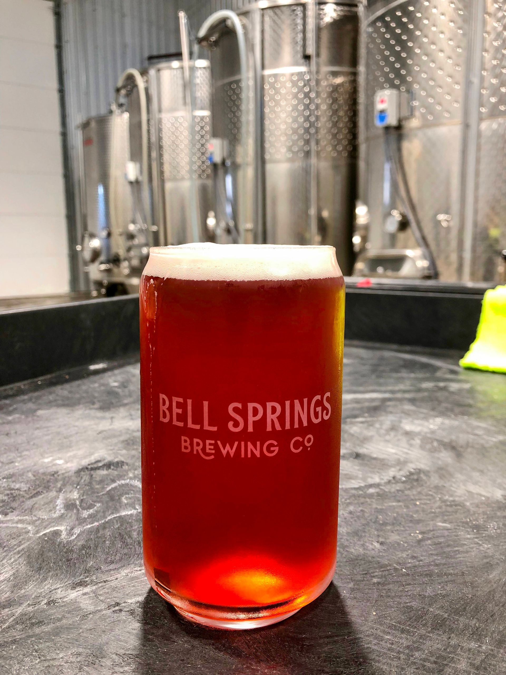 Glass of red beer from Bell Springs Brewing Co. in front of brewing tanks.