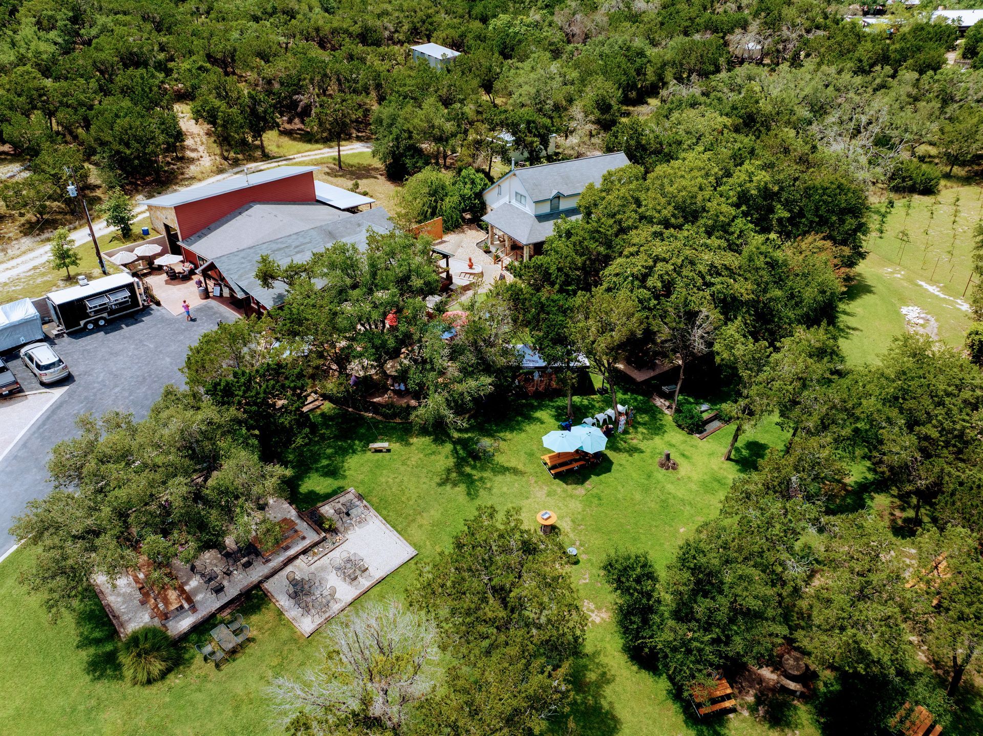 Aerial view of a red building, trees, and grassy area with tables and seating.
