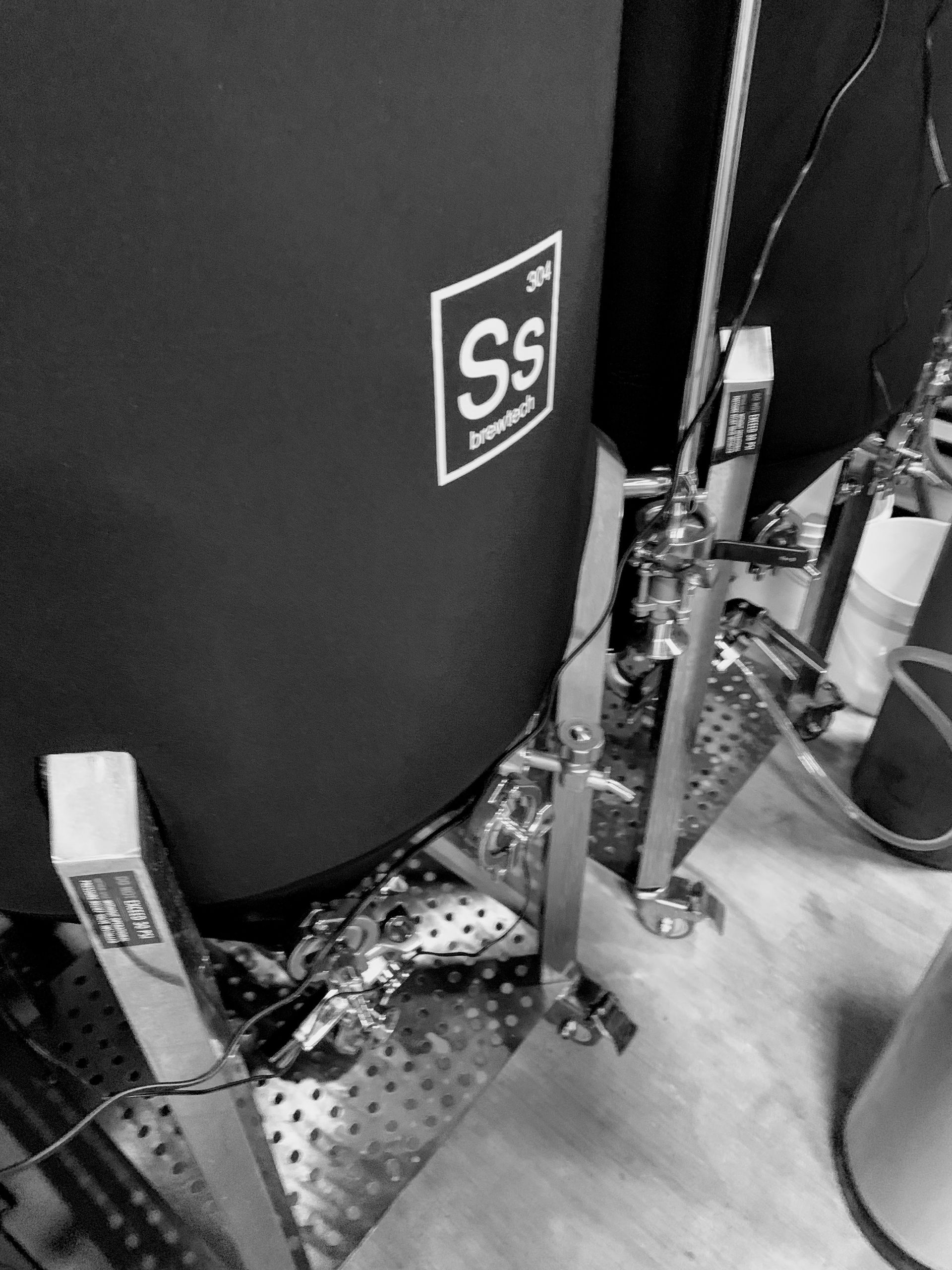 Black and white close-up of a drum set. The drum has a logo with the letters