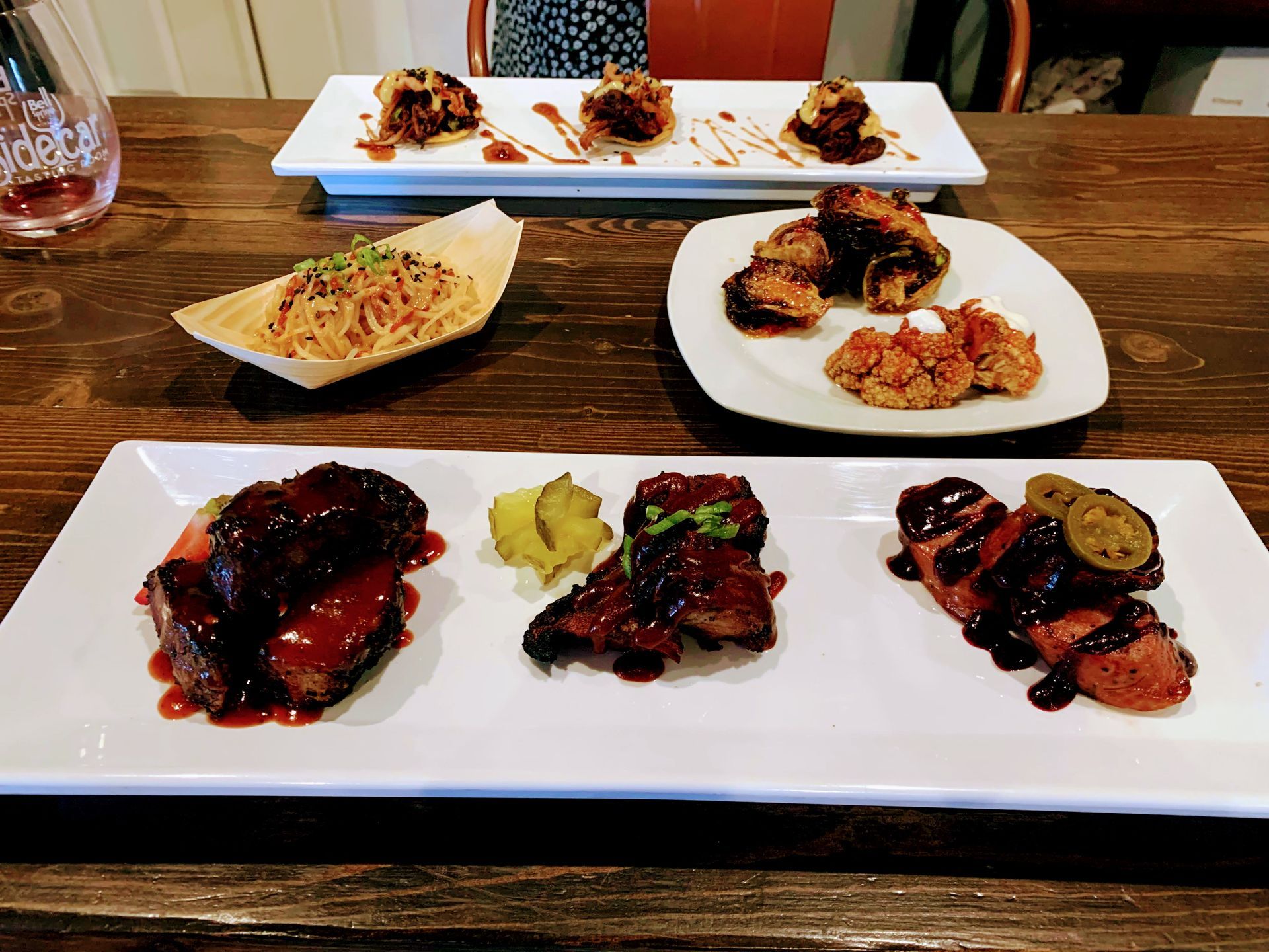 Various small dishes on white platters, including fried foods with dark sauces, on a wooden table.