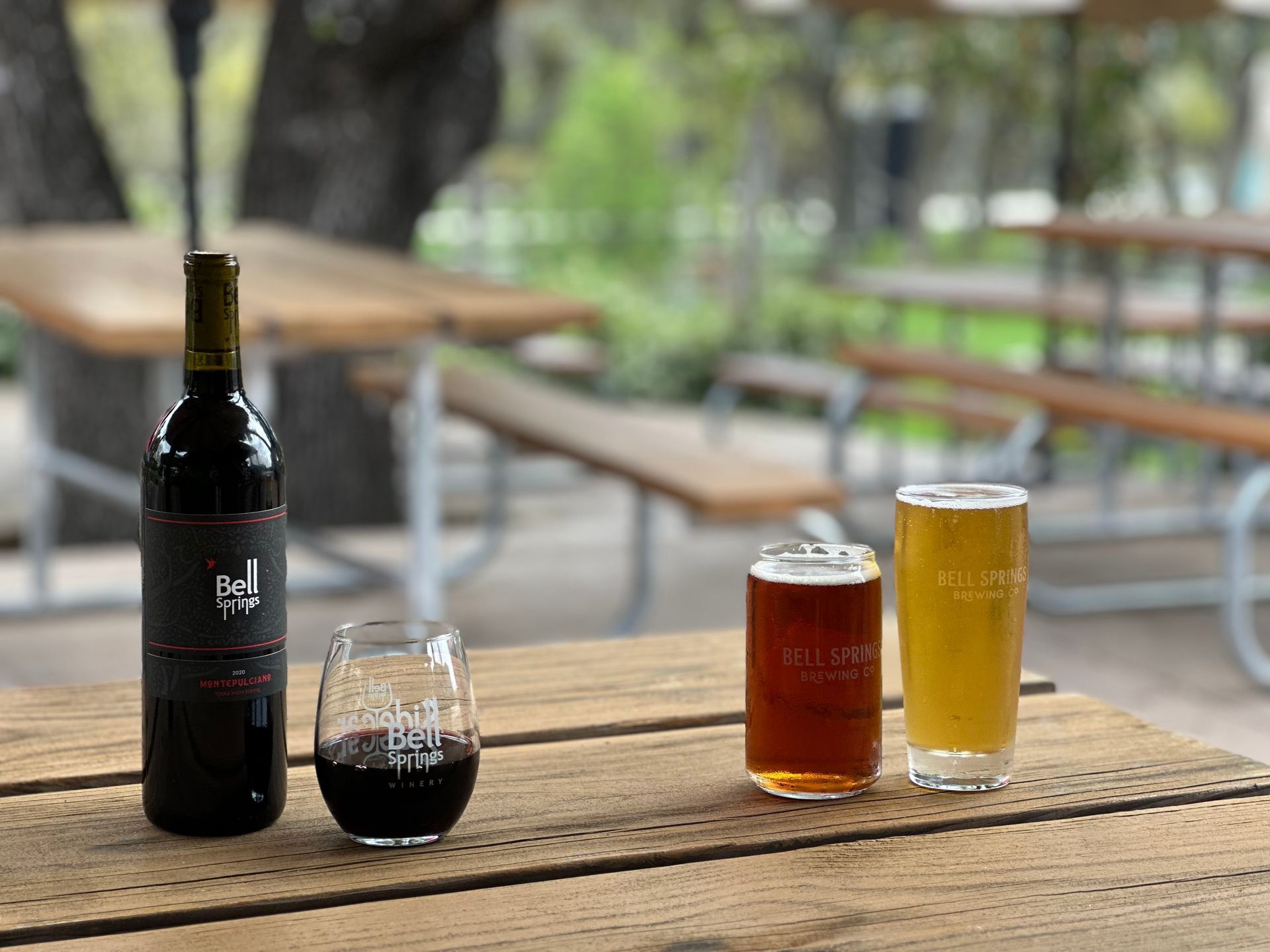 Bottle of red wine with wine glass, two beers, outdoor table.