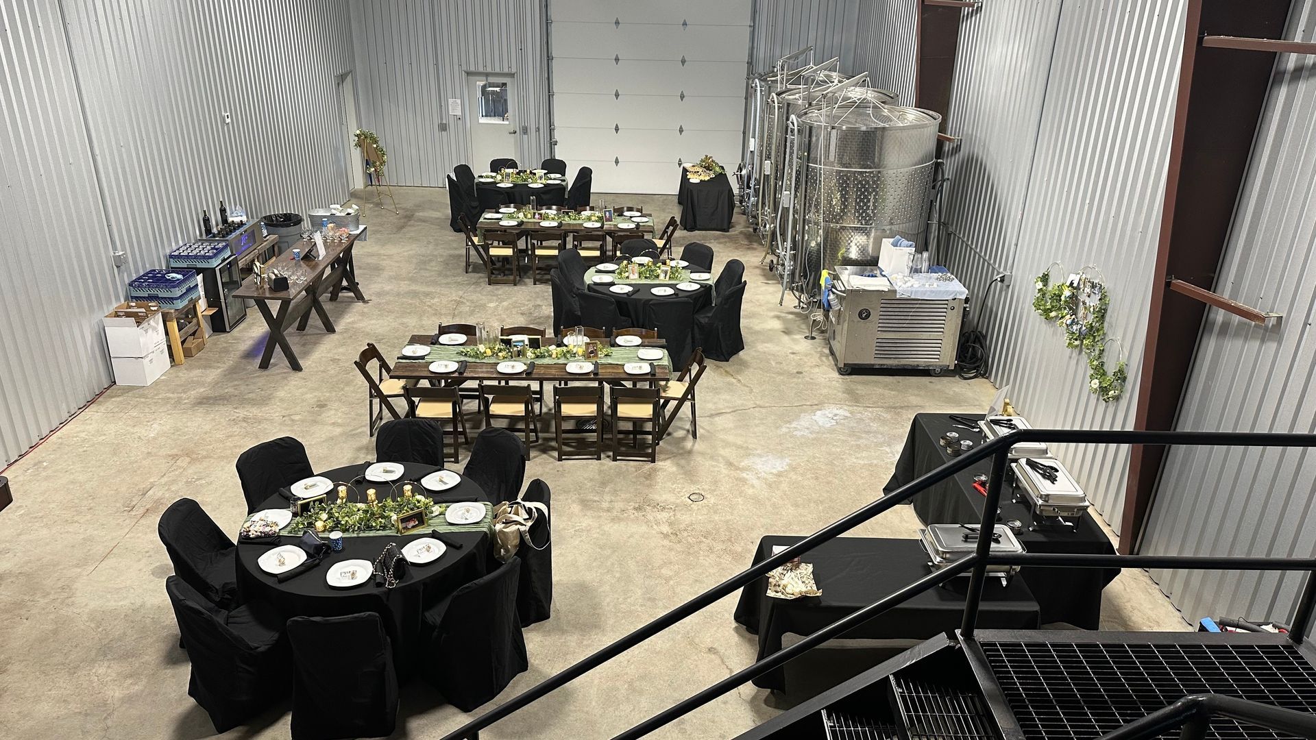 Tables set for an event in a metallic, industrial-looking room. Some guests are in the background.