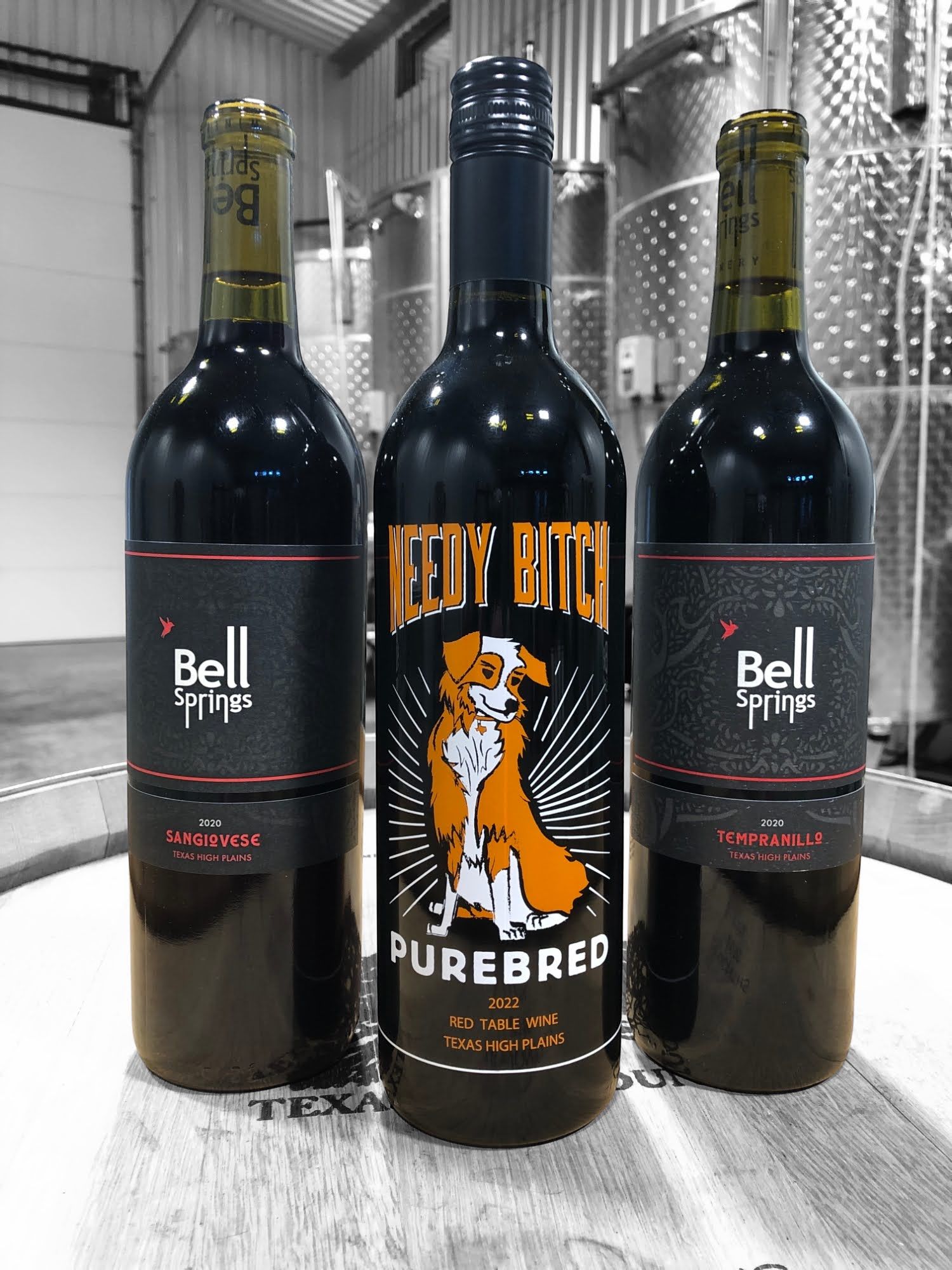 Three dark bottles of wine on a wooden surface.