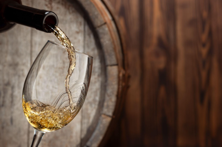 White wine being poured into a glass, barrel in background.