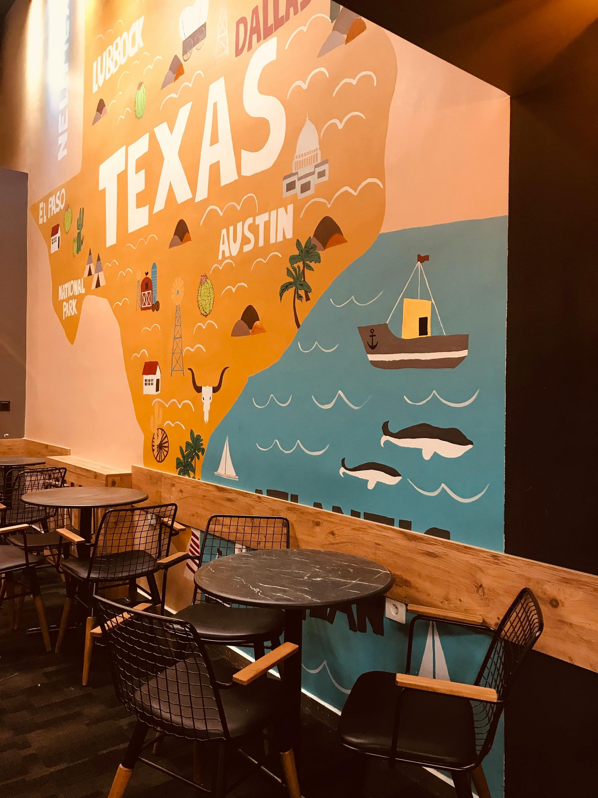 Mural of the state of Texas with illustrations, in a cafe setting, with tables and chairs.