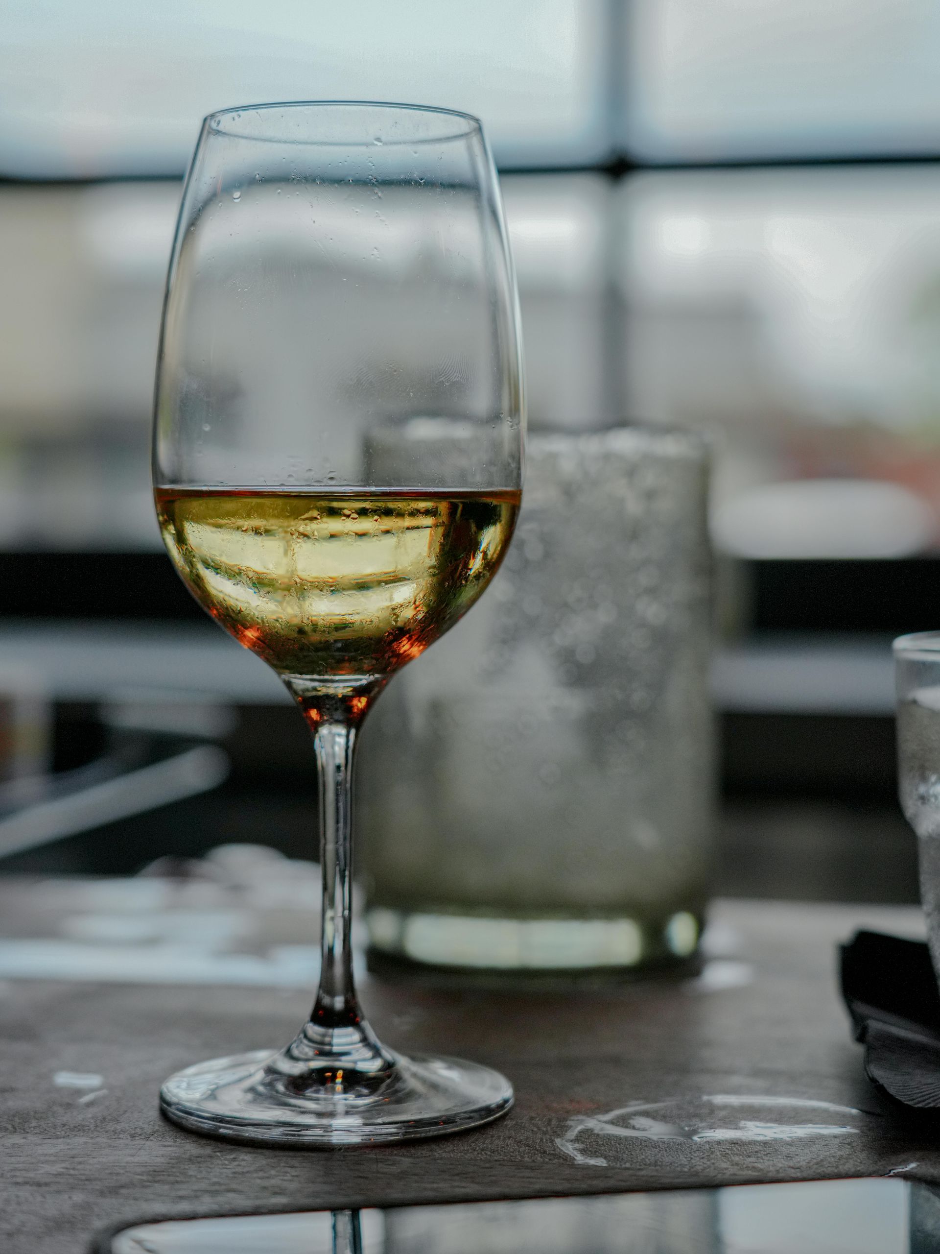 Glass of Texas white wine on a table, next to a candle holder, against a blurry background.