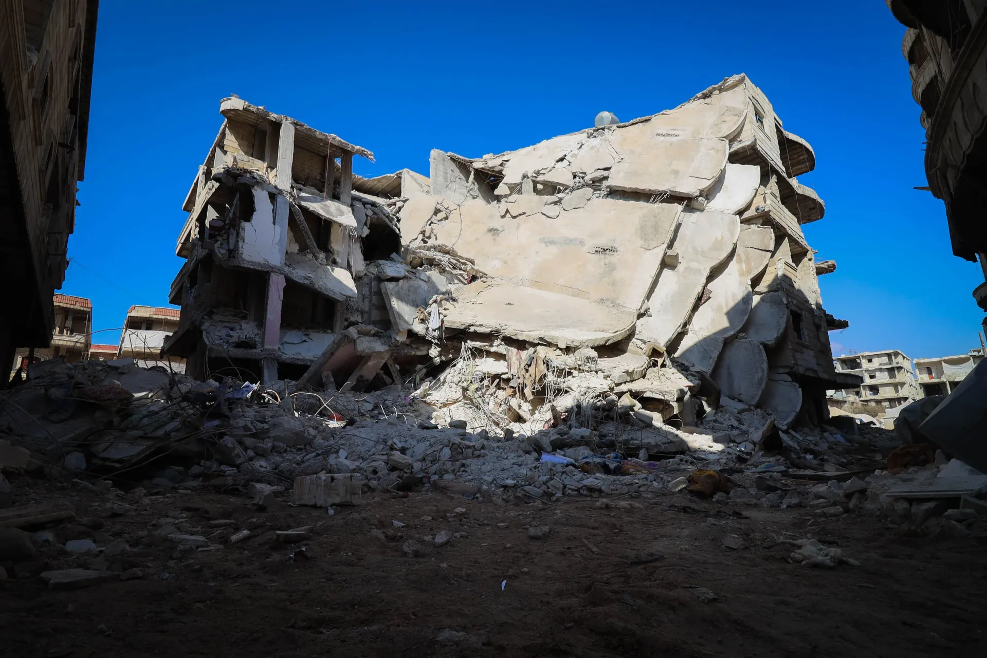 Collapsed concrete building rubble under a bright blue sky
