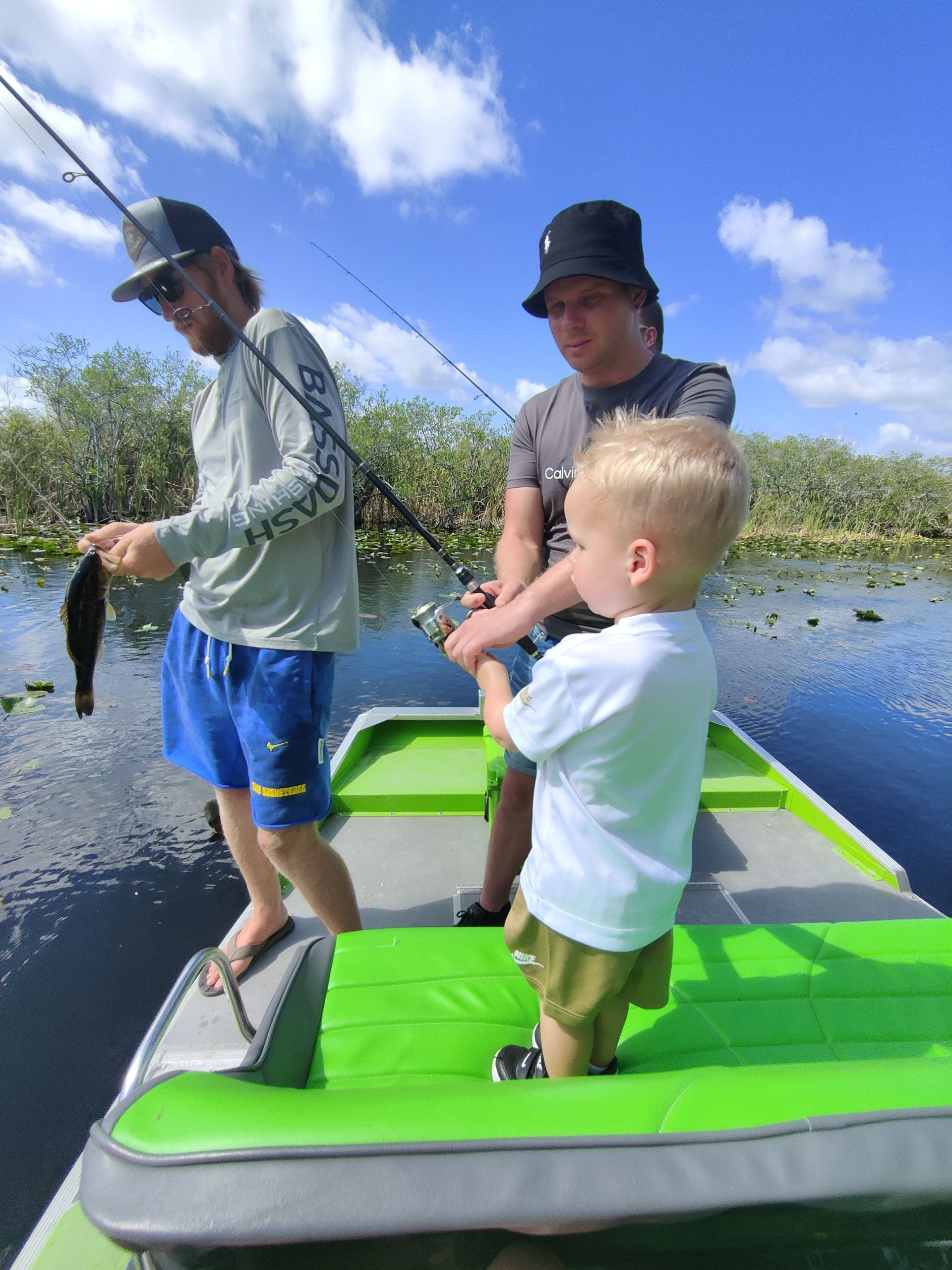 Three people fishing from a boat on a lake; one holds a small fish.