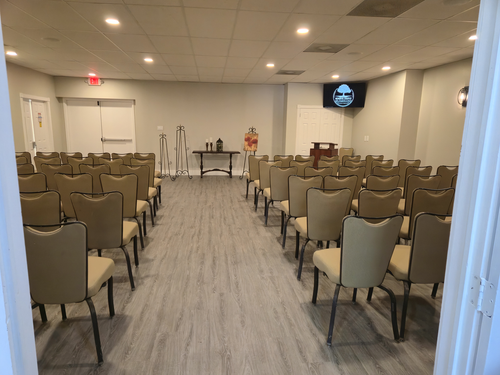 Empty conference room with rows of tan chairs facing a stage and screen.