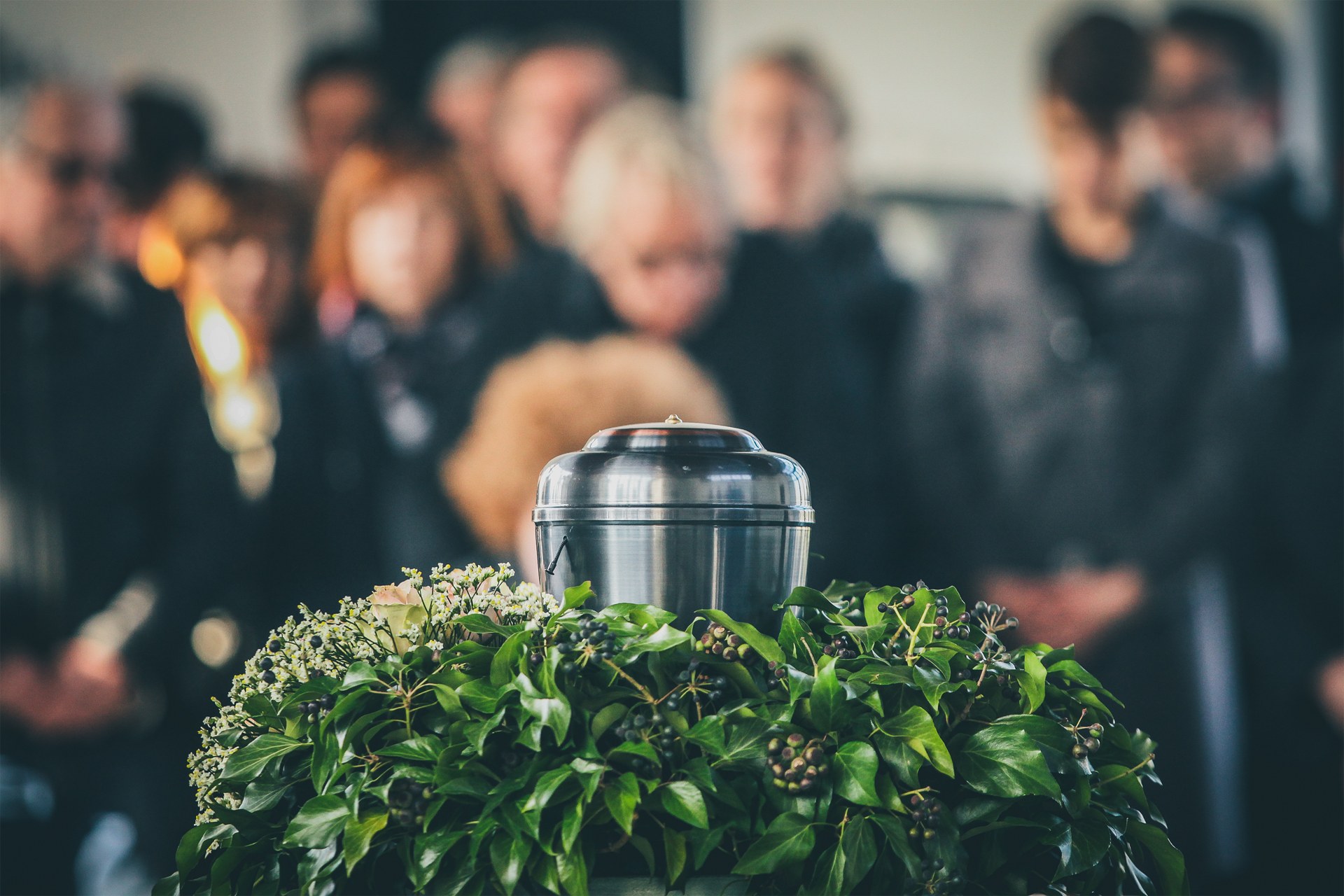 Silver urn on a green wreath with blurred people in the background