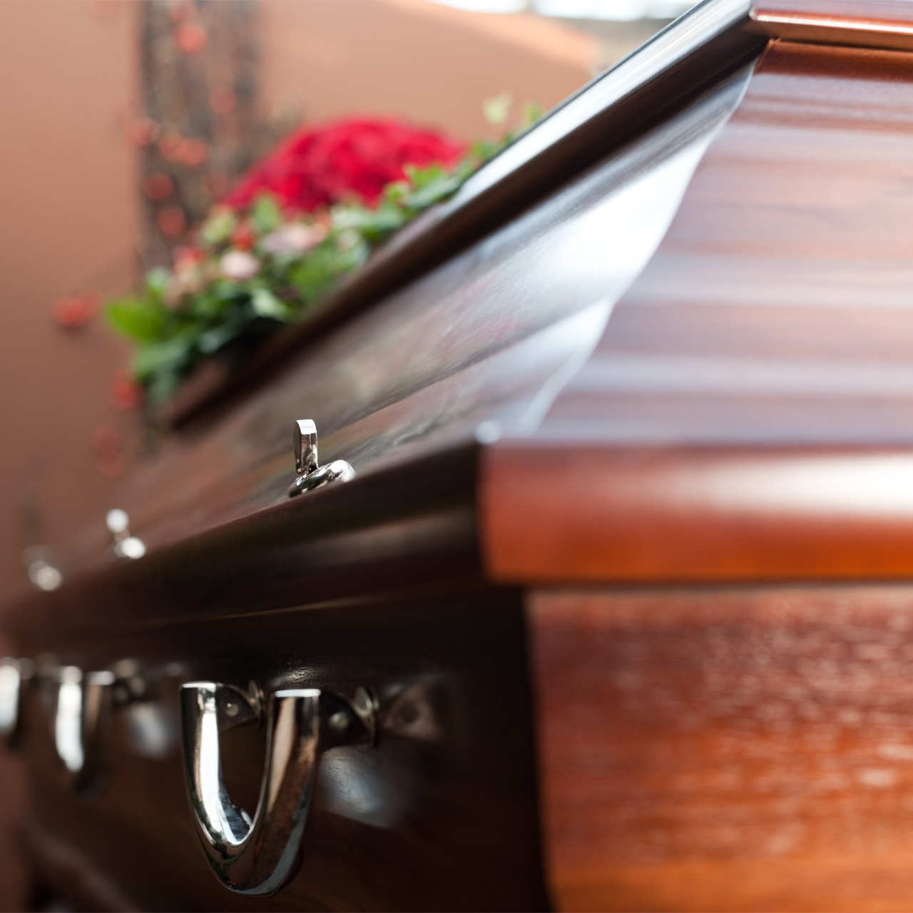 Open casket at a funeral, with white satin lining and red flowers in the background