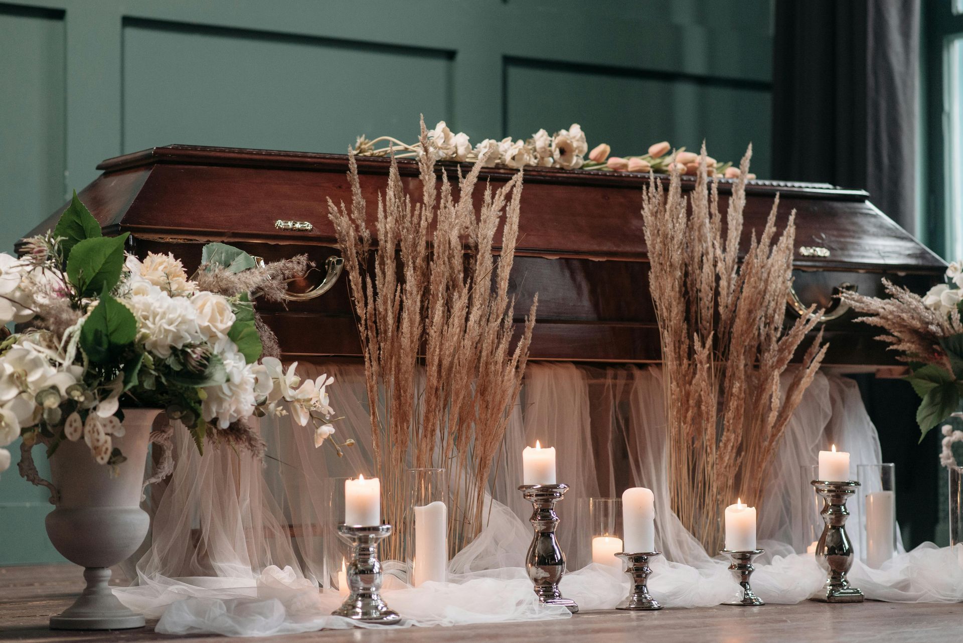 Wooden casket with floral arrangements and lit candles on a memorial table